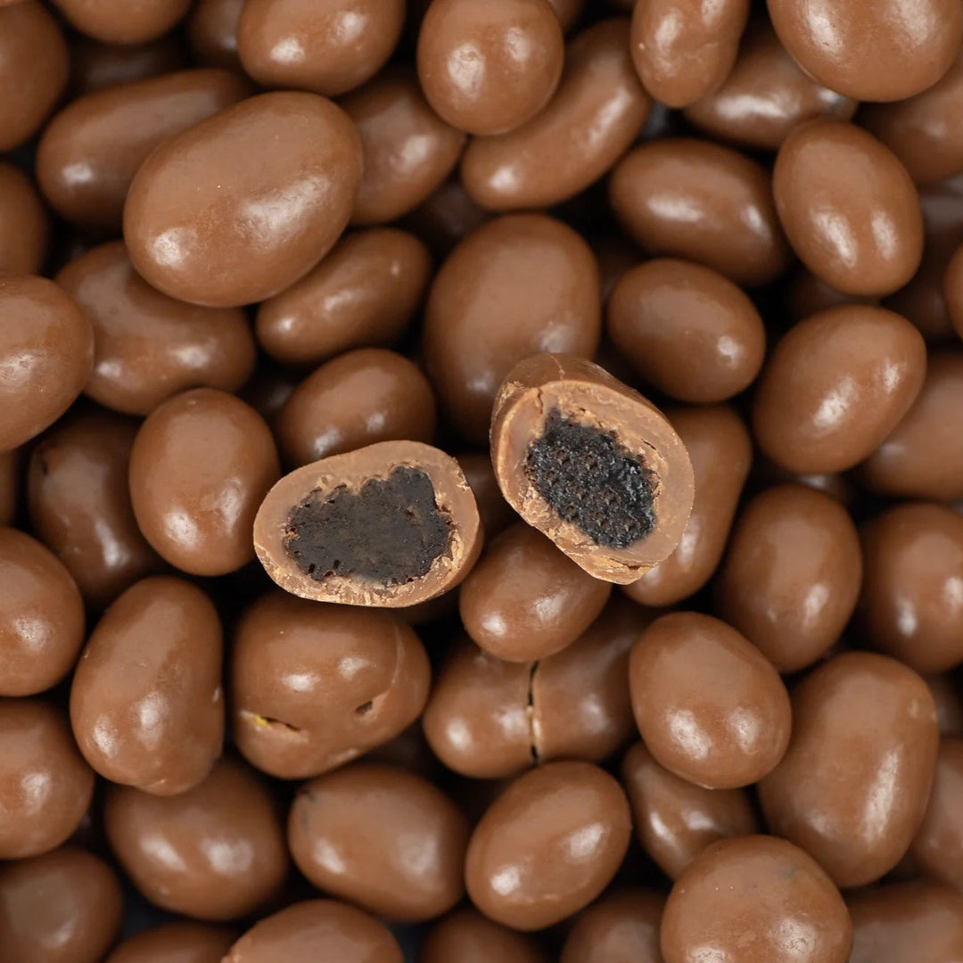 A close-up of glossy brown chocolate-coated candies, with two pieces broken open to show a dark chocolate center, filling the frame.