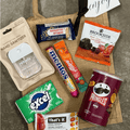 Box of Snack Delights Snack Bag by Gift Smack Gift Company, featuring a variety of colorful snack items arranged in a clear box.
