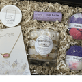 Gift set with candle, lip balm, bath bombs, and body butter in a box.