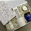 Gift box with a floral notebook, candle, mug, and jar of tea on a wooden surface.