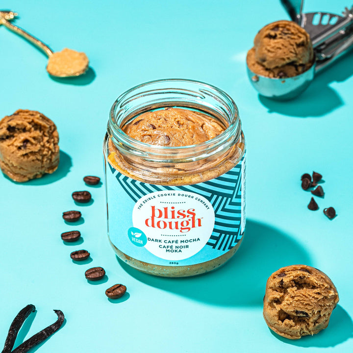Jar of 'bliss dough' cookie dough cream with cookies and coffee beans on a blue background