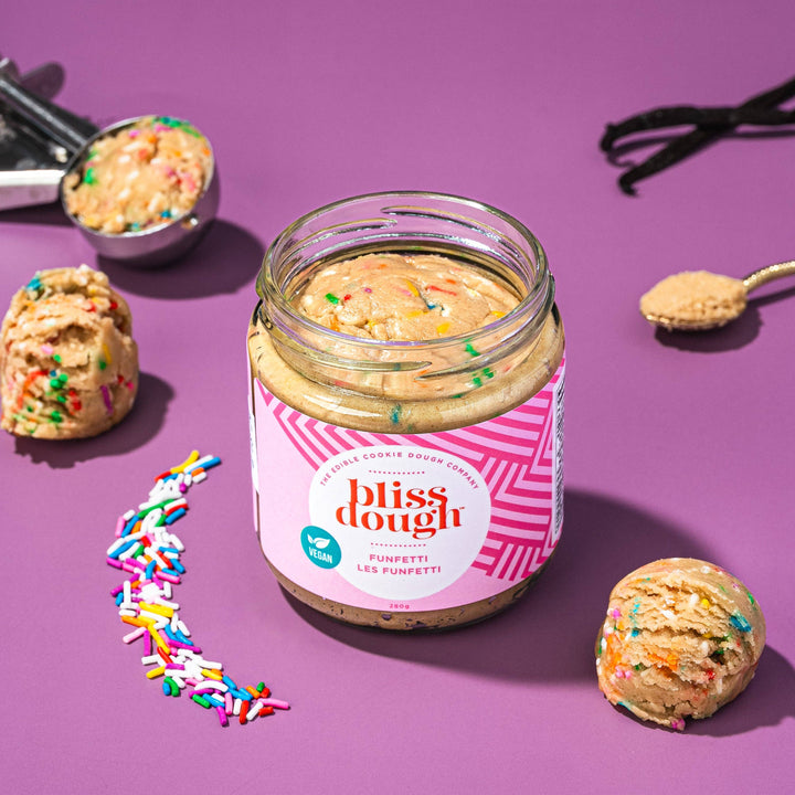 Jar of bliss dough with sprinkles on a purple background
