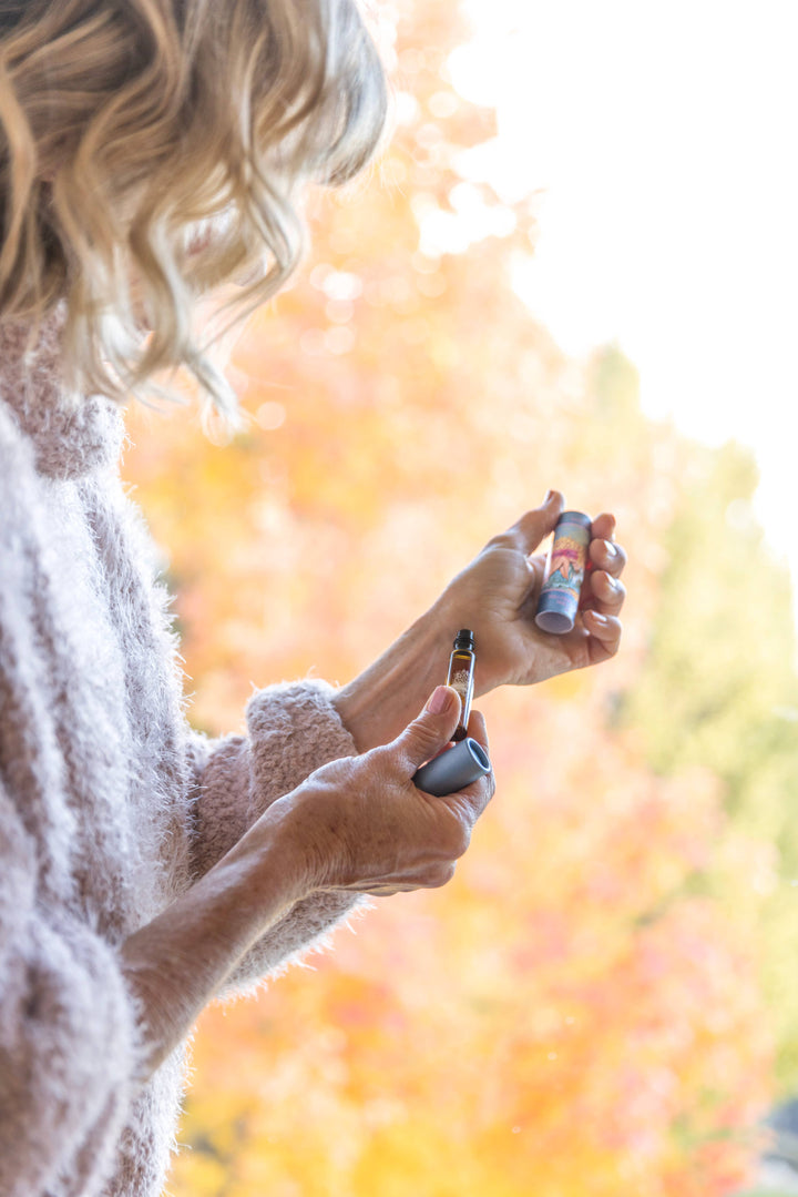 Person holding two lip balms with a blurred autumn background
