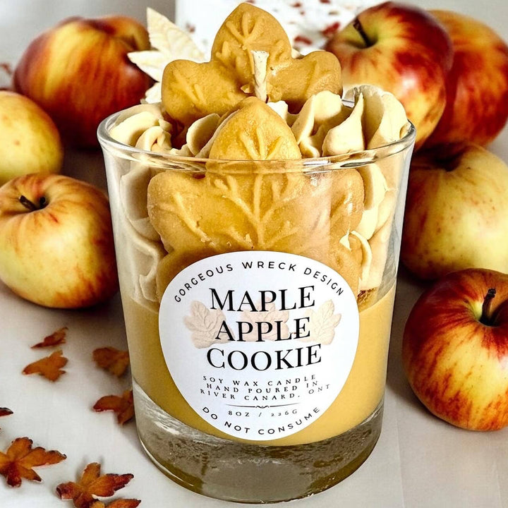 Maple apple cookie candle in a glass jar with apples and autumn leaves around it.