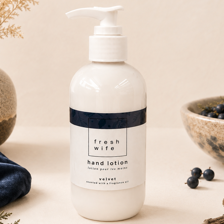 A bottle of Fresh Wife hand lotion in the velvet scent, styled on a neutral beige surface with dried flowers, a blue velvet cloth, and blueberries in rustic ceramic bowls.
