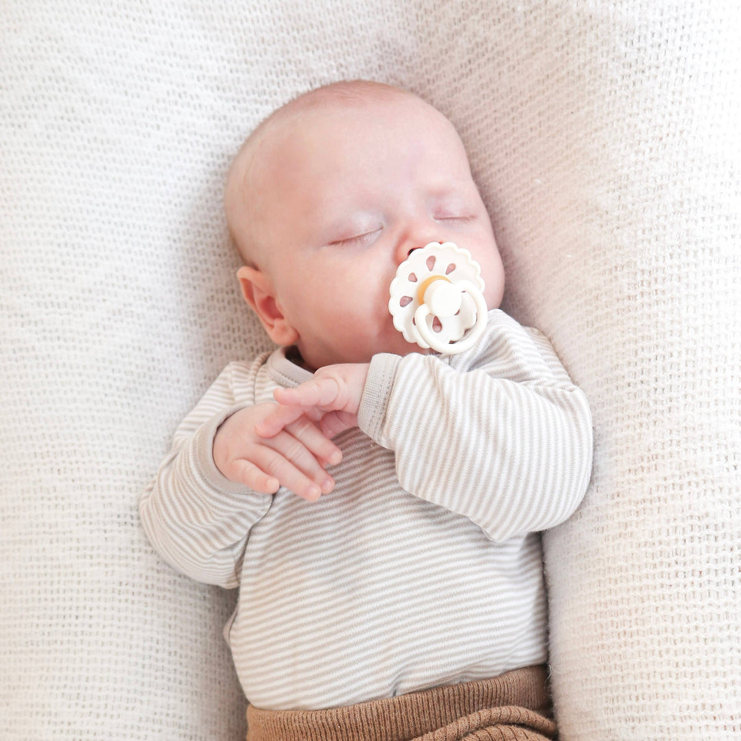 Baby sleeping with a white pacifier on a soft beige blanket