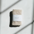 Agha exfoliating bath mitt for body cleansing, showing textured fabric for removing dead skin during shower or bath.
