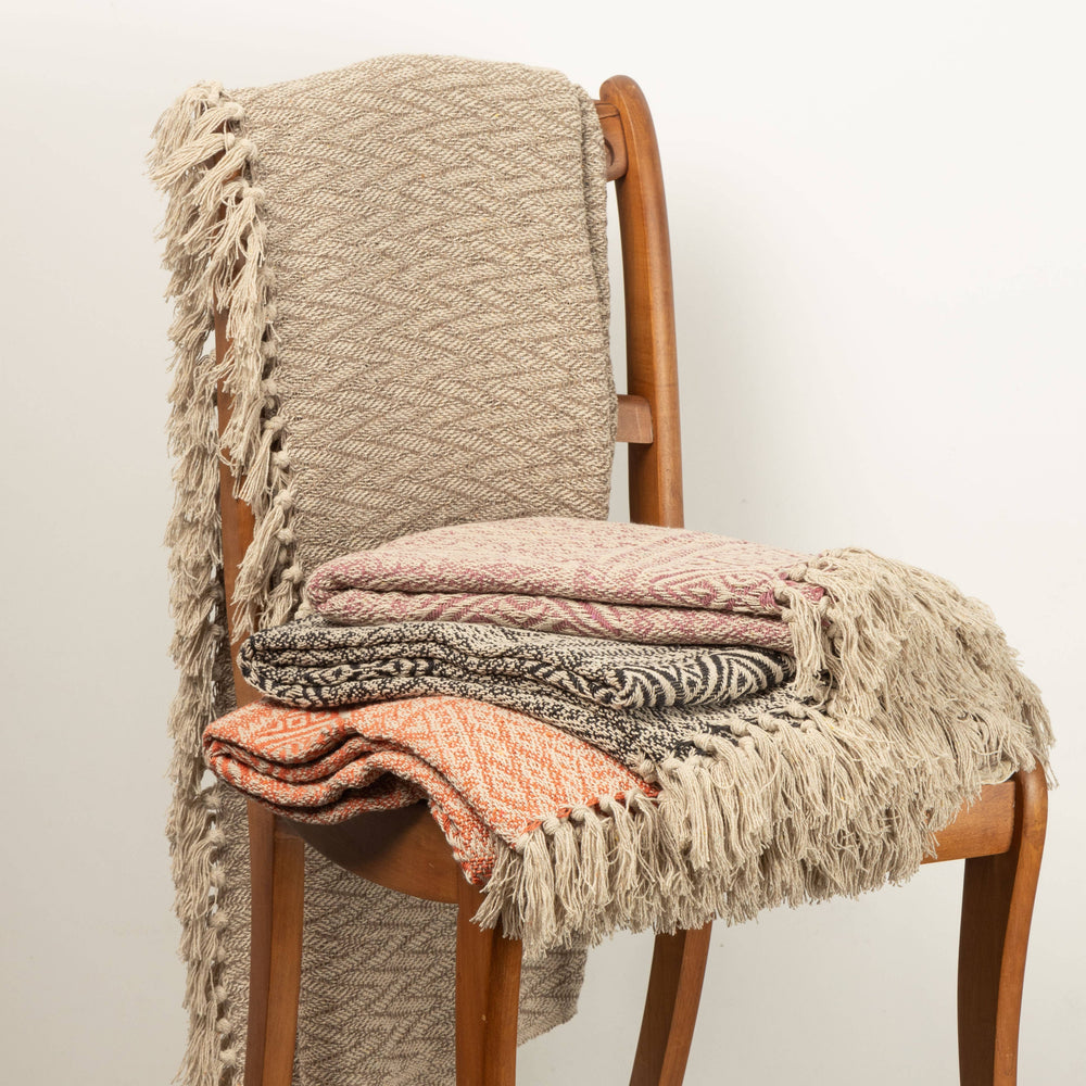Stack of patterned blankets on a wooden chair against a plain background