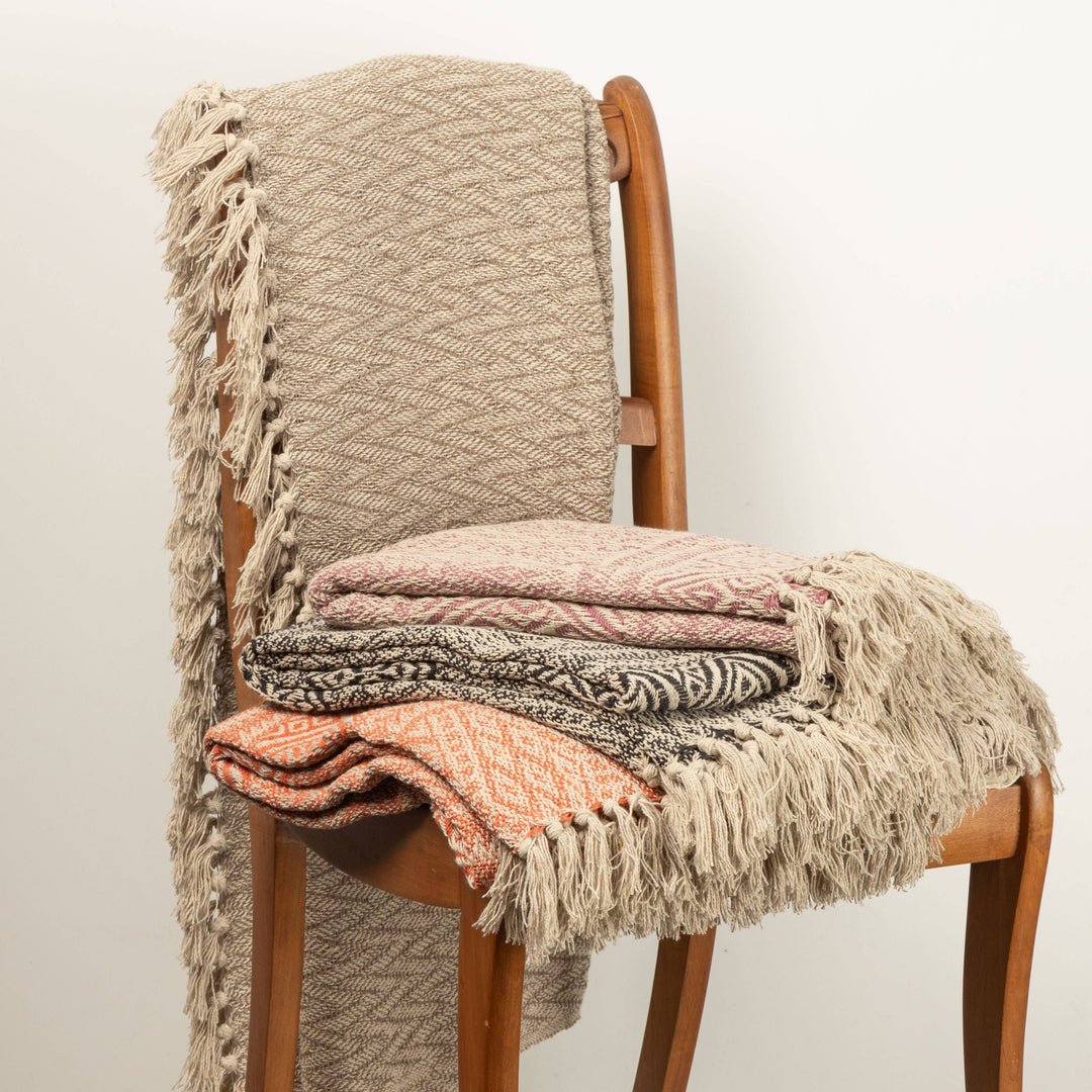 Stack of patterned blankets on a wooden chair against a plain background