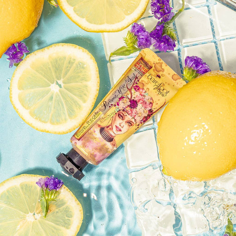 Lip balm with floral packaging surrounded by lemon slices and purple flowers on a blue tiled background