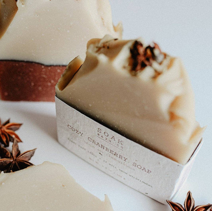A close-up of a handmade soap bar in a white paper sleeve labeled &