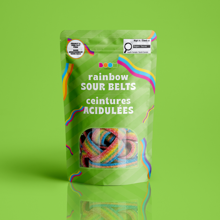A stand-up pouch of rainbow sour belts candy on a bright green background. The packaging is light green with colorful wavy lines and white text reading &