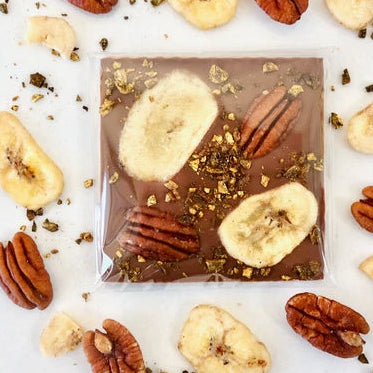 Chocolate bar with banana slices and pecans on a white background