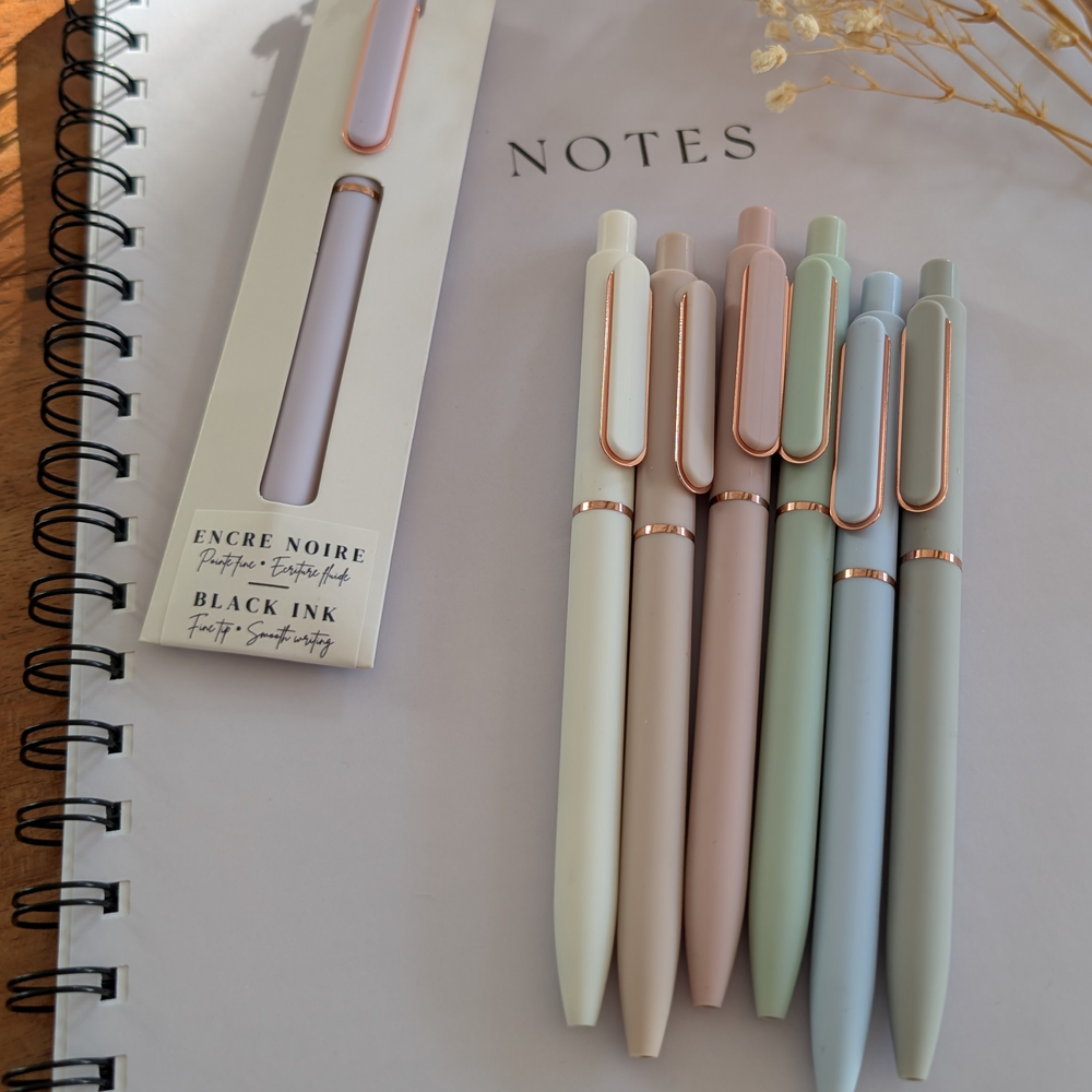 Set of pastel-colored pens with rose gold accents on a notebook titled 'NOTES'.