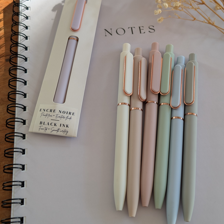 Set of pastel-colored pens with rose gold accents on a notebook titled &