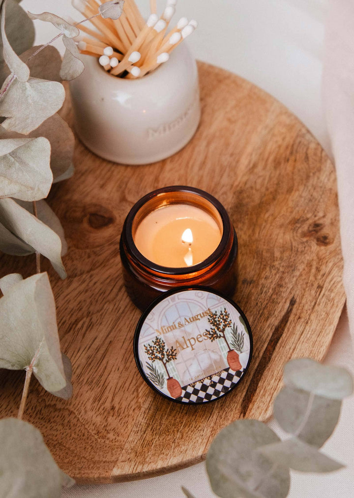 Candle in a decorative container on a wooden surface with eucalyptus leaves.
