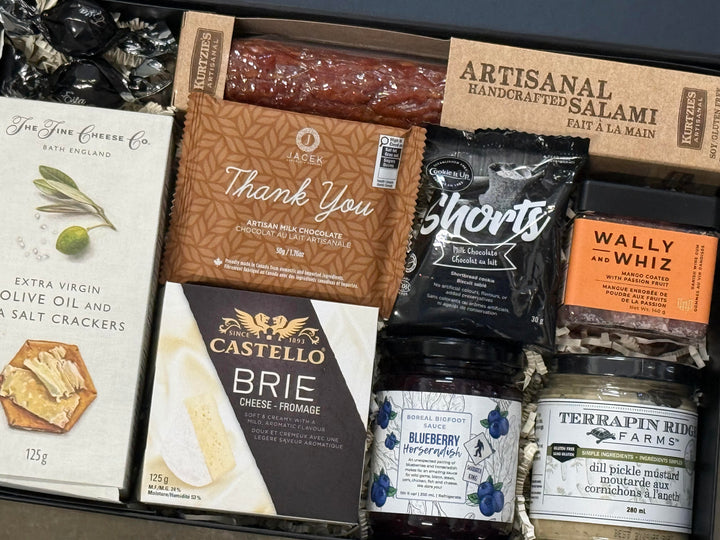 Assorted gourmet food items including cheese, salami, and pickles in a box.