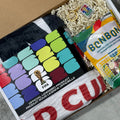 Box containing socks, a bag of candy, and a keychain with colorful branding.